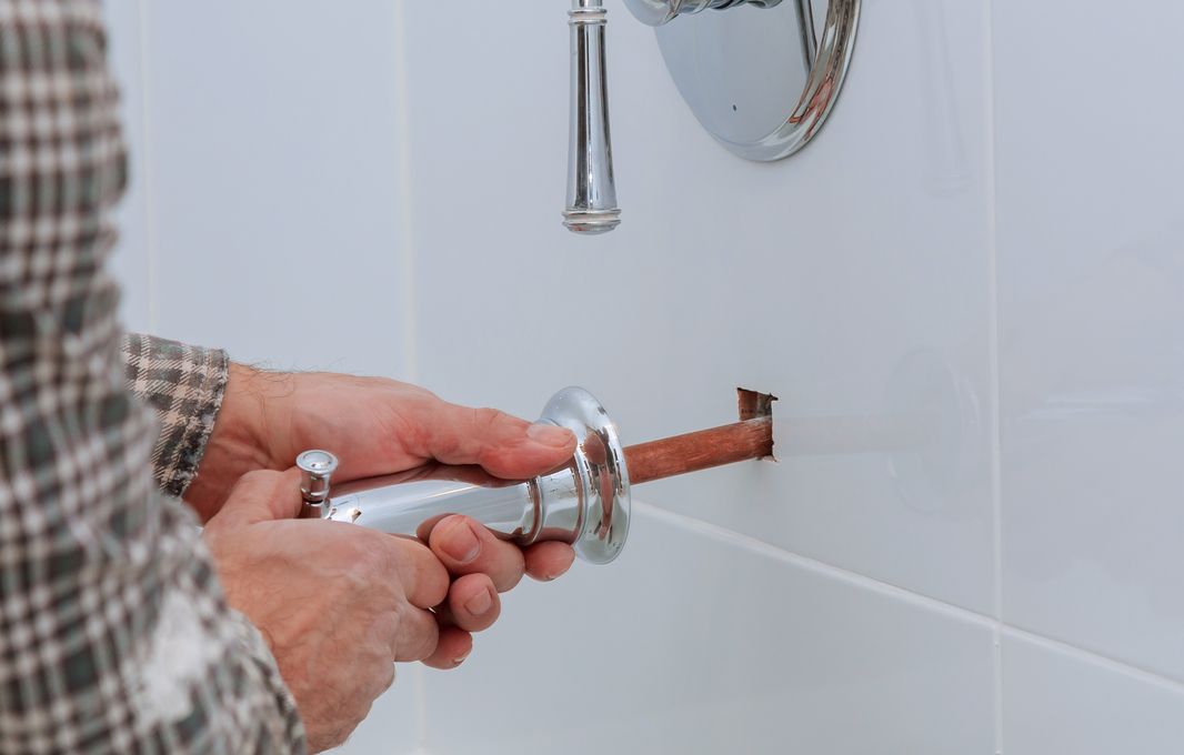 Plumber fitting a pipe stub in a white-tiled bathroom wall