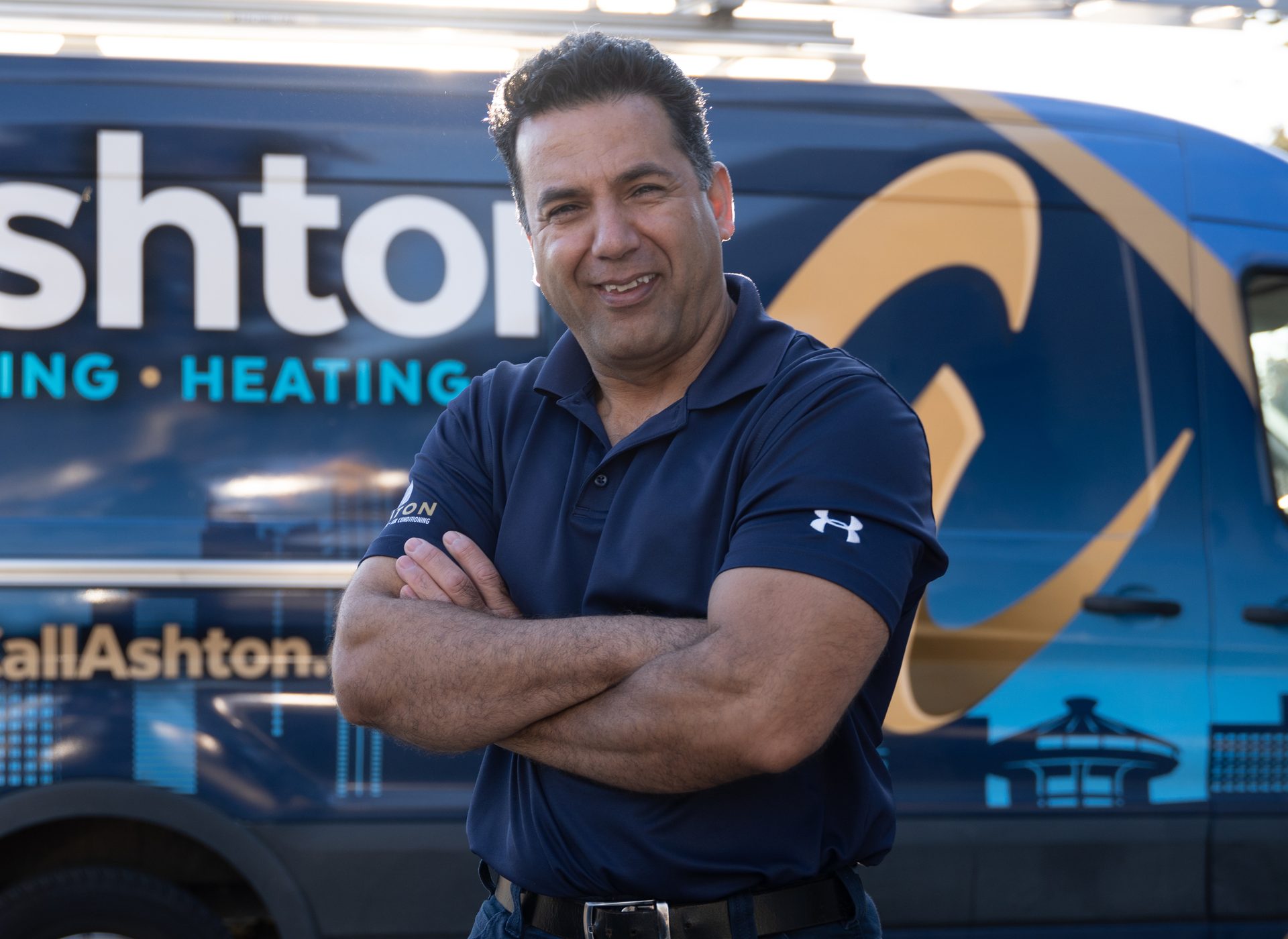Smiling Ashton technician with his arms crossed in front of an Ashton service van